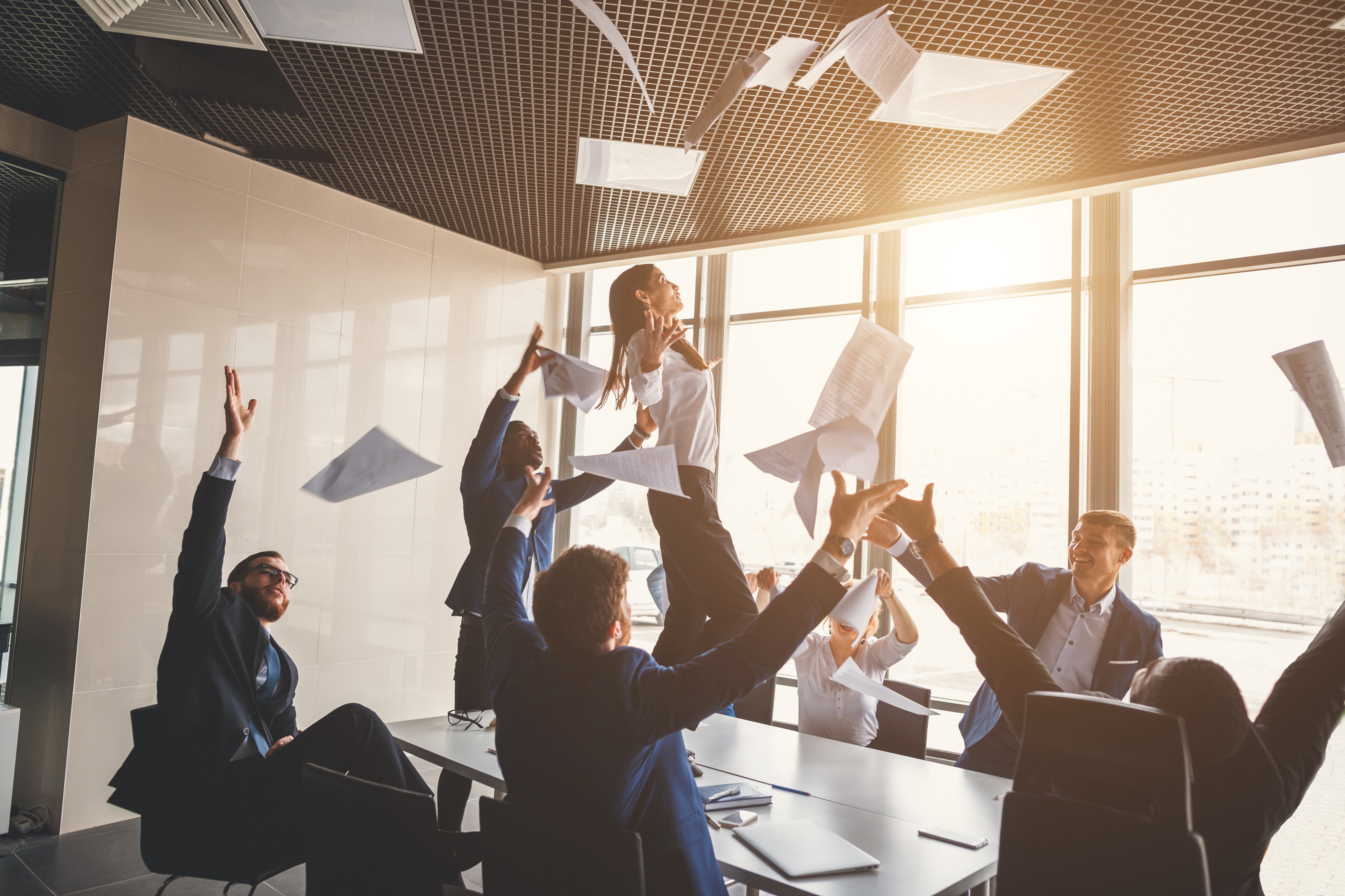 employees in meeting room celebrating and throwing papers